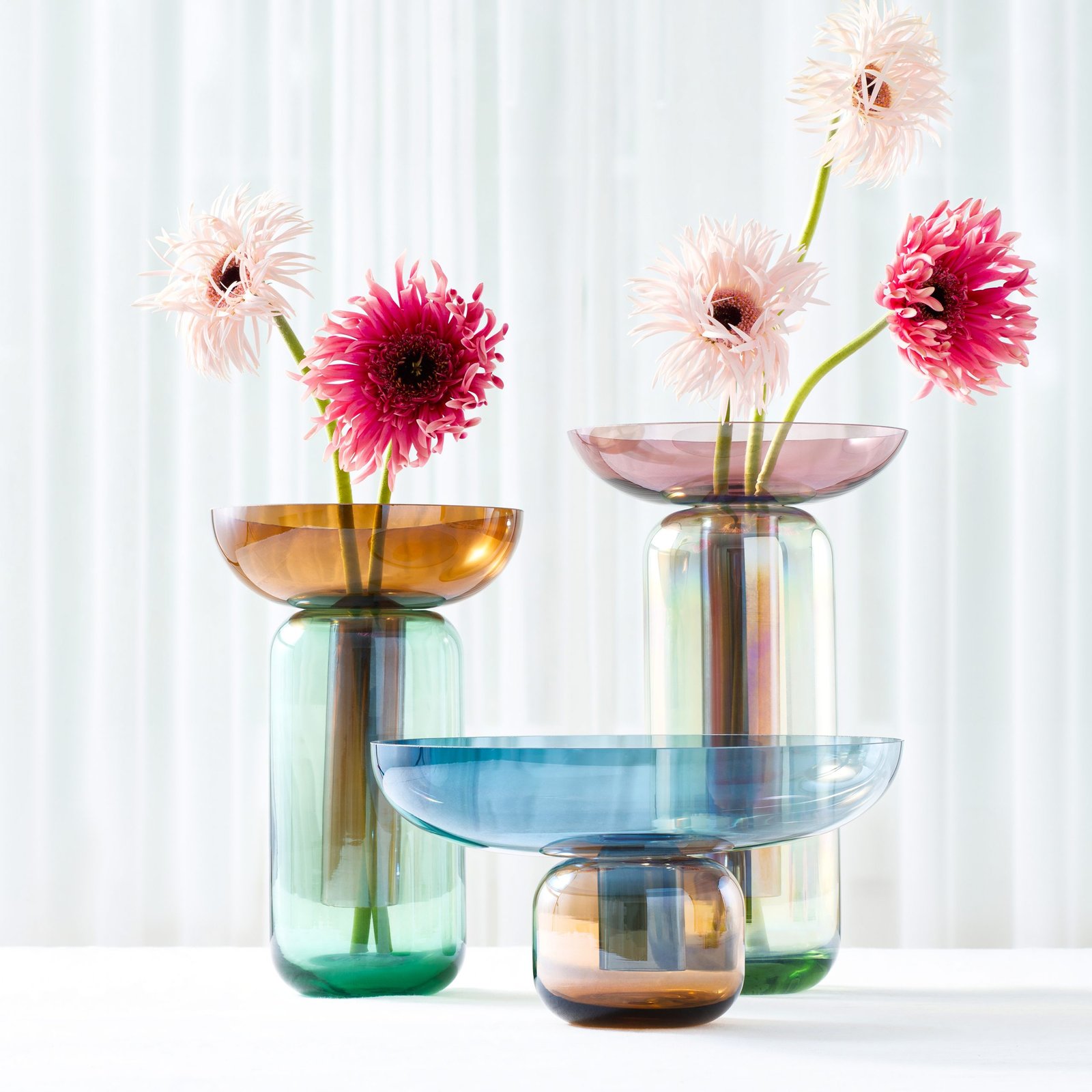product lifestyle photography of colored glass vases with flowers on white table cloth