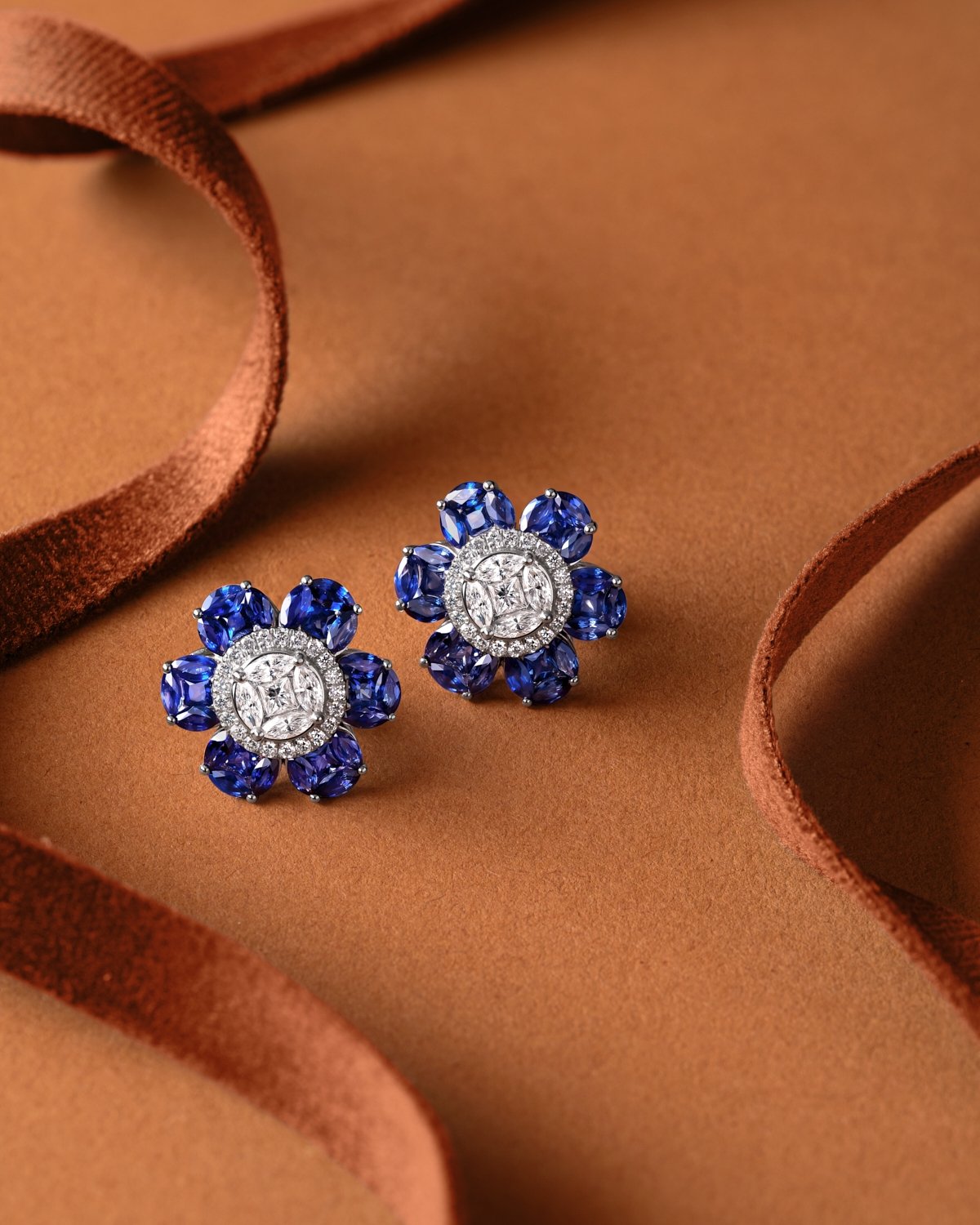 product lifestyle photography of diamond and blue sapphire earrings on clay colored background with red ribbons
