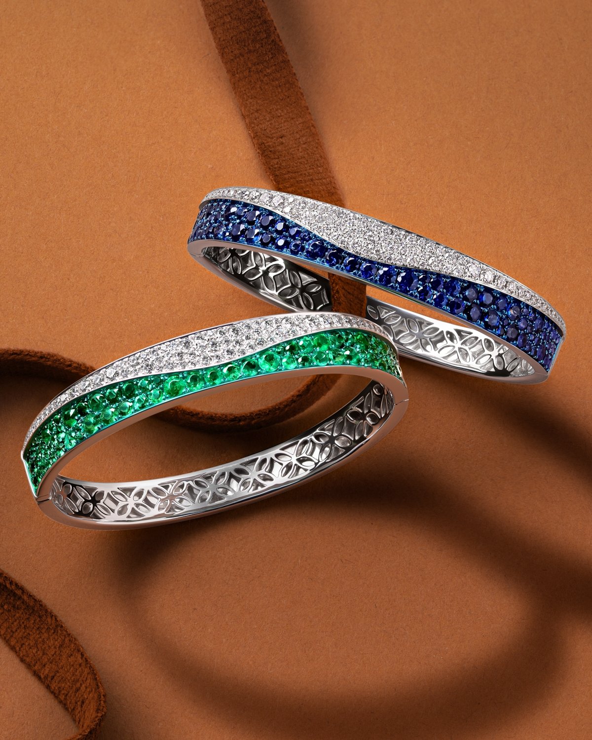 product lifestyle photography of diamonds and blue sapphire green sapphire bracelets on clay colored background with red ribbons