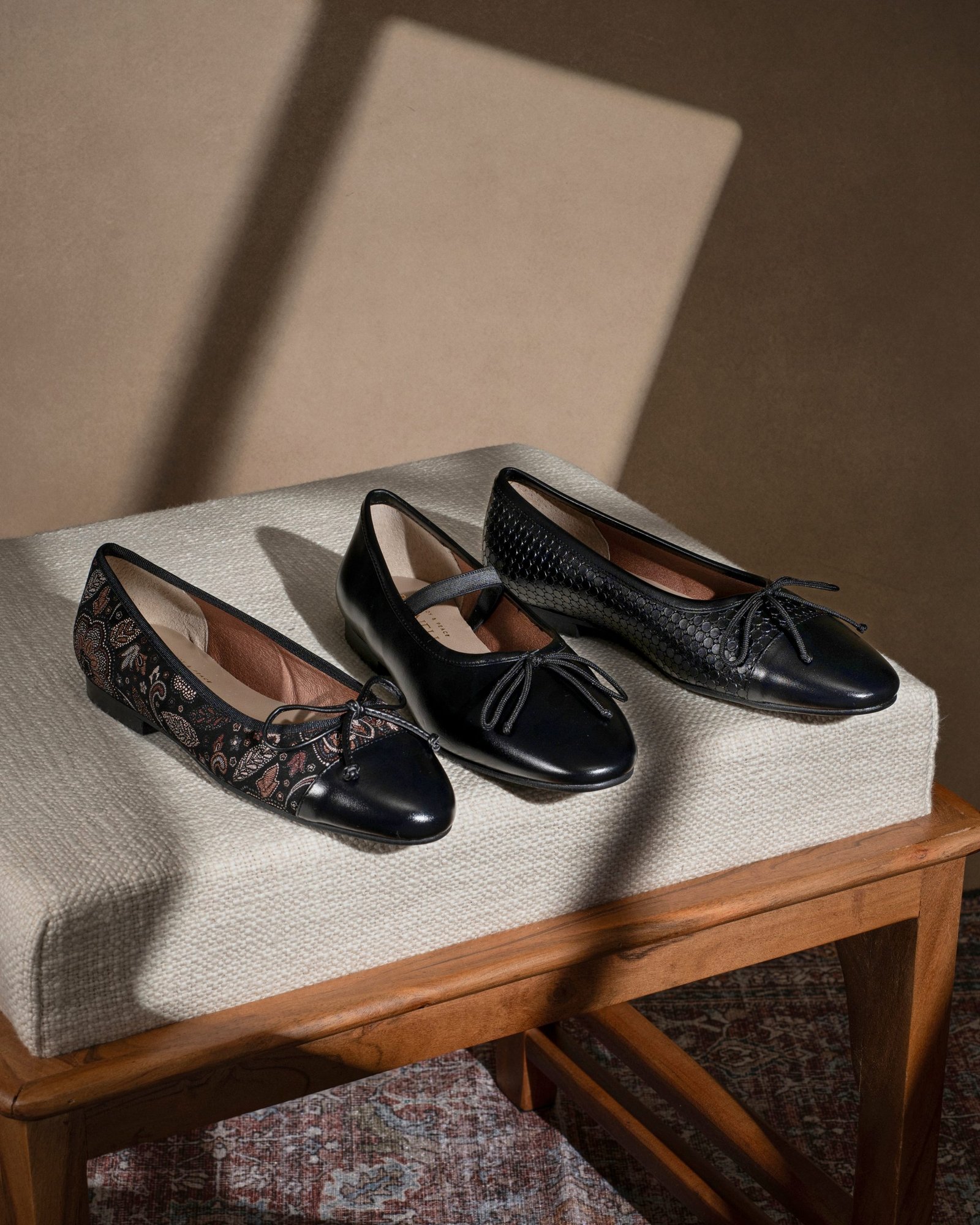 product lifestyle photography of black and floral patterned women's shoes on tan seat cushion chair with shadows