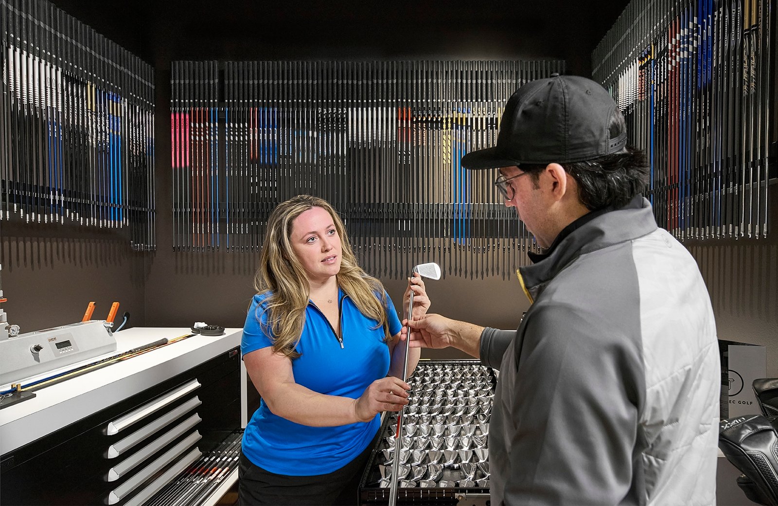 product lifestyle photography of true spec golf, indoor golf club fitting with female student and male instructor exchanging golf club