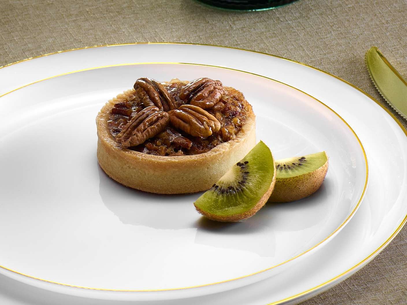 product lifestyle photography of white dinner plates with gold trim, pecan pie with kiwi on plate