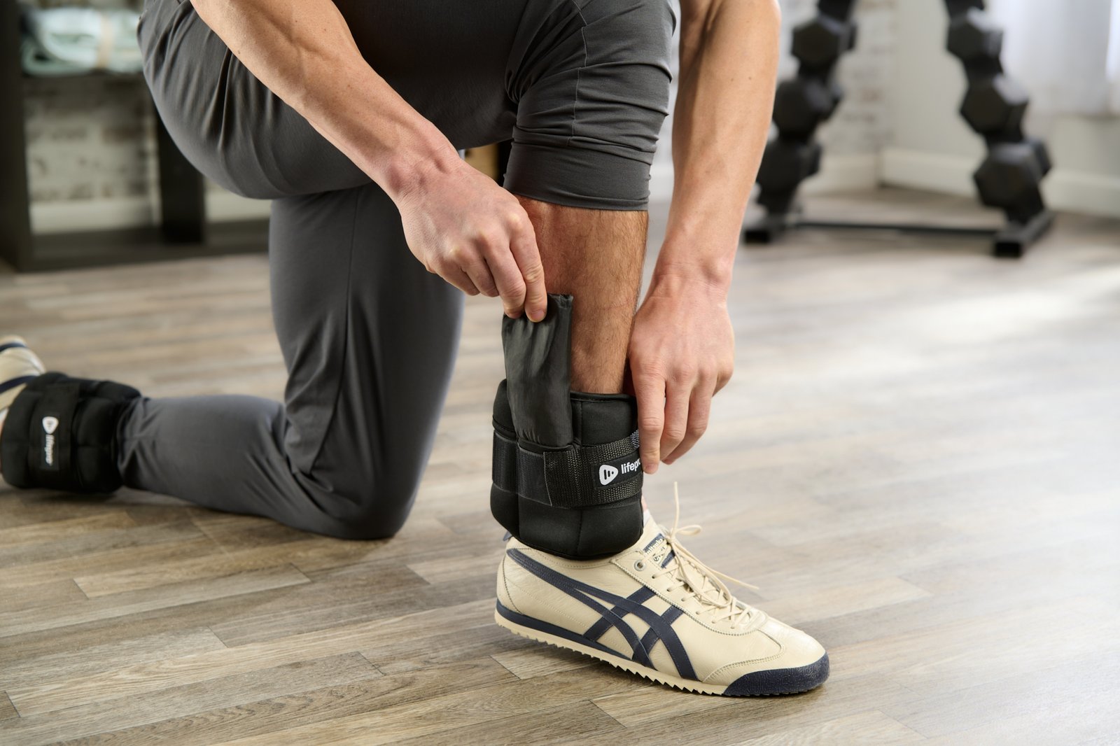 product lifestyle photography of male model in room set with ankle weight around ankle kneeling while placing weight inside of product